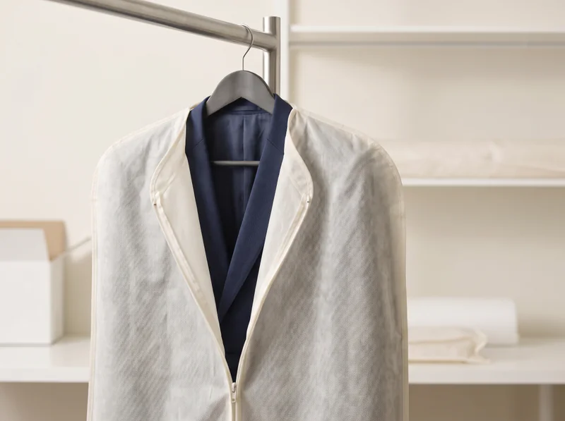 Navy jacket on a hanger inside a partially unzipped ivory garment cover.